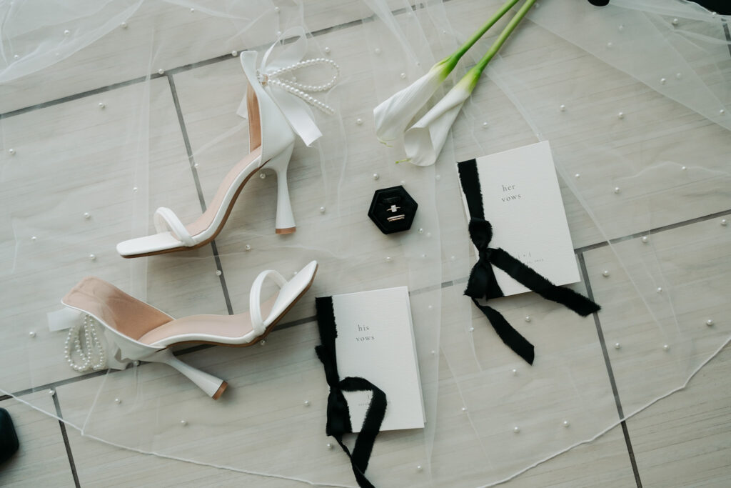 Modern and elegant wedding details of the bride's shoes, veil, vows, bouquet, and rings.