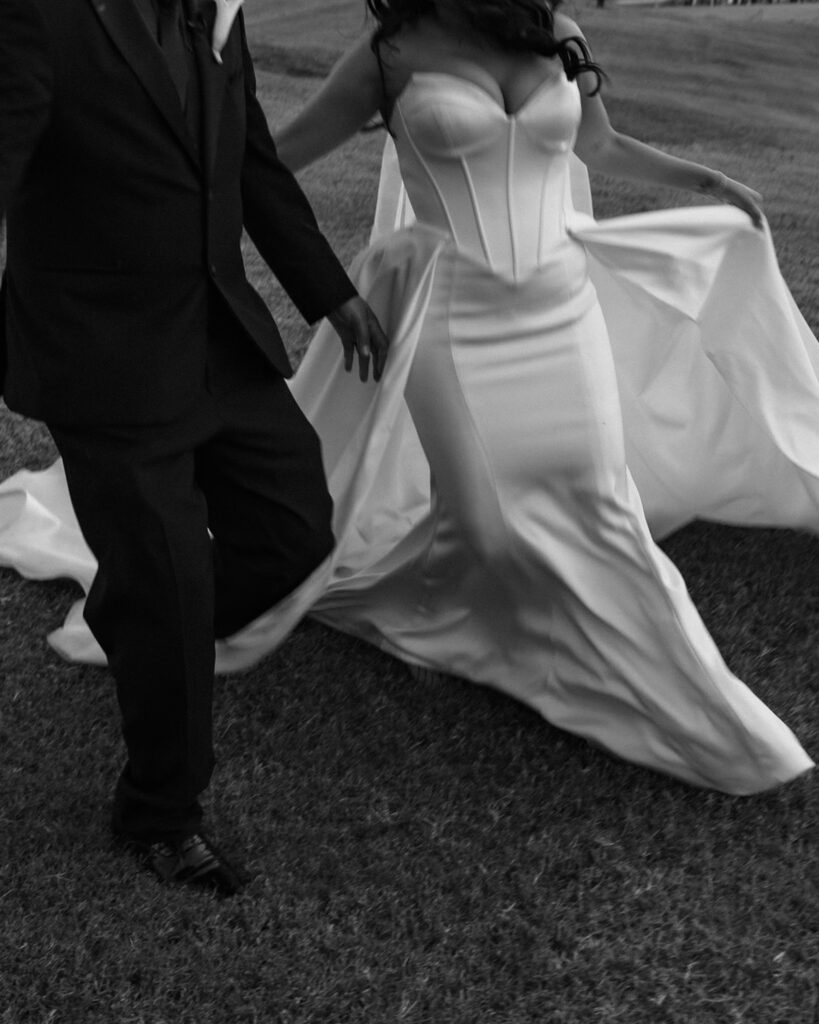 Bride and groom walking together up a grassy hill beneath a large tree at sunset during their Arizona wedding photos.