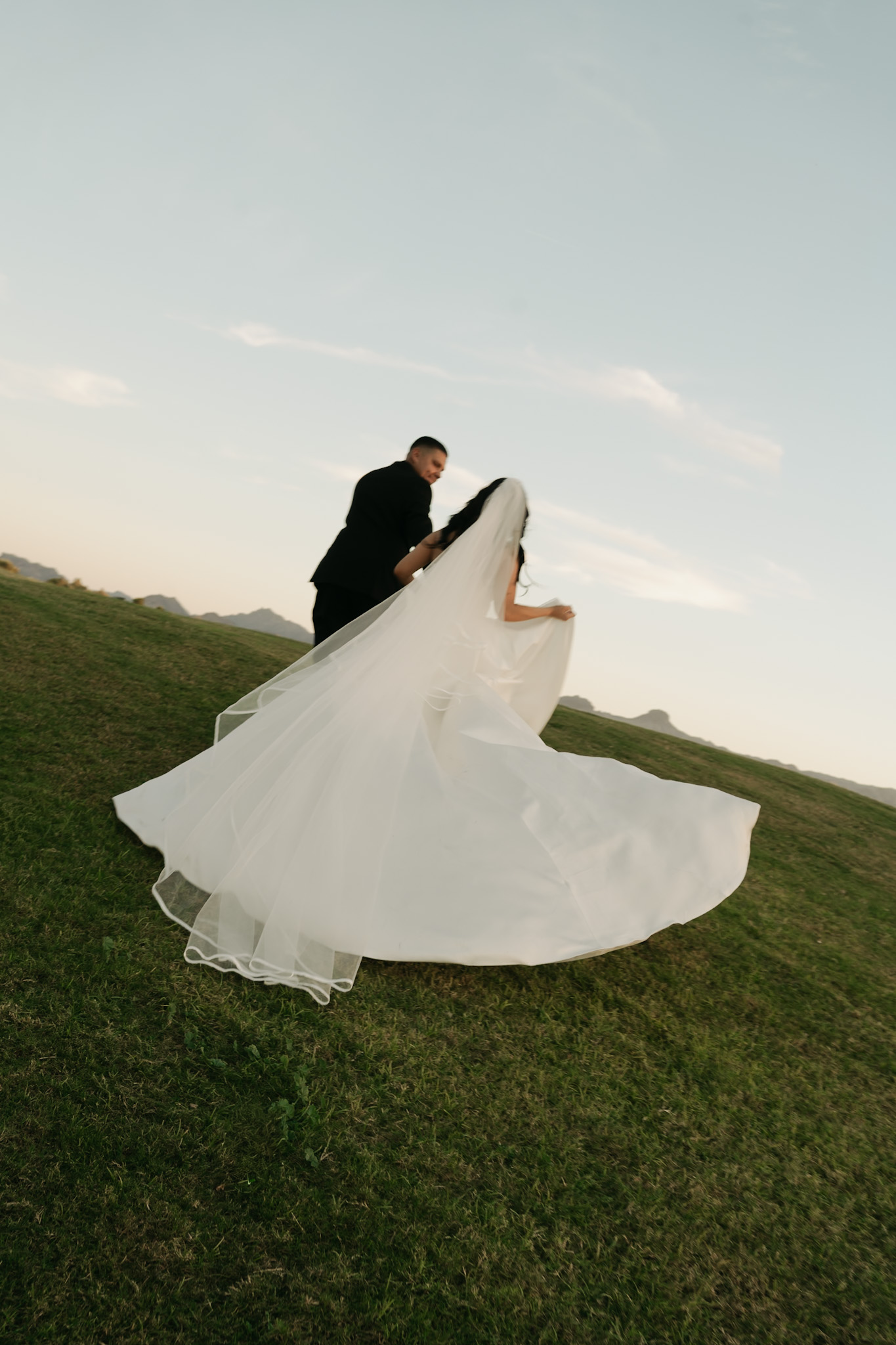 Bride and groom running together up a grassy hill with cinematic light during their Arizona wedding photos.