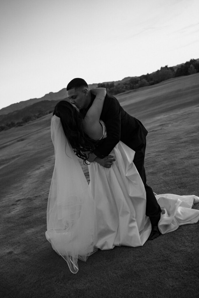 Bride and groom dancing together up a grassy hill beneath a large tree at sunset during their Arizona wedding photos.