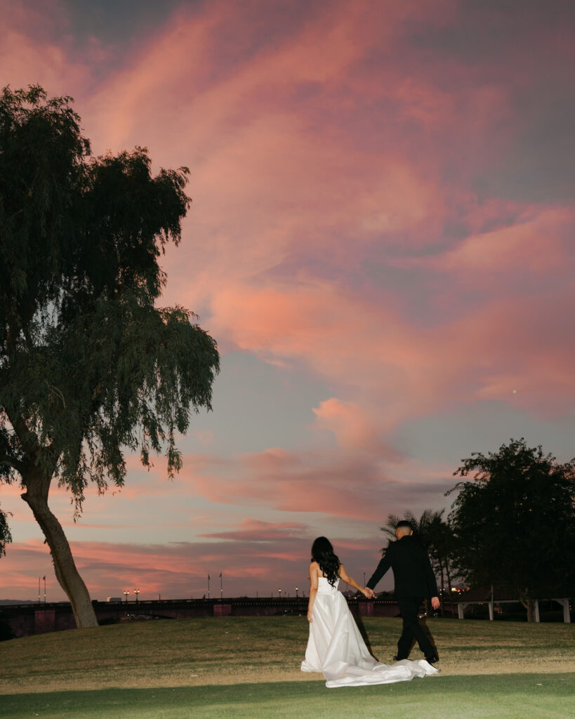 Bride and groom holding hands at dusk under a pink sunset sky at their Arizona wedding near the London Bridge.