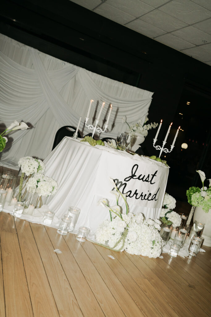 A “Just Married” sign layered with white florals and champagne glasses at a modern Arizona wedding.